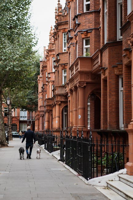 A detailed exterior view of a multi-storey residential building with red brick facades and white accents, featuring numerous large sash windows and black wrought iron balconies. The building's surface