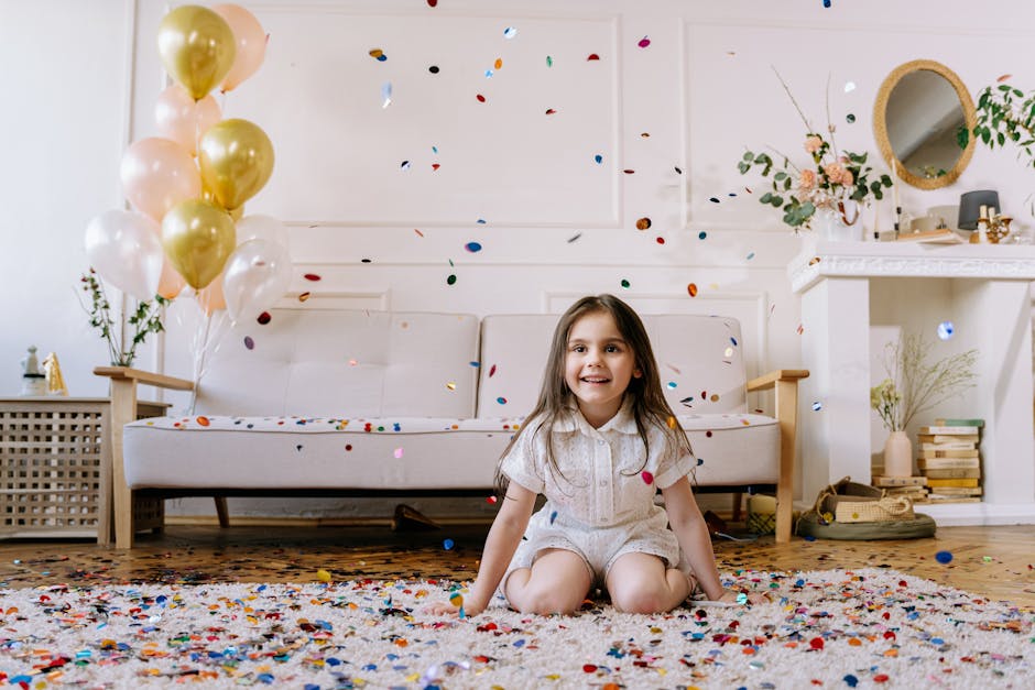 A person is cleaning a light-colored wooden floor in a room decorated for a celebration or party, with gold confetti scattered across the surface. The individual is barefoot, and only their lower legs and feet are visible, wearing a sparkly dress. They are using a broom to sweep up the confetti, which is collected in a dustpan placed on the floor. The room features natural light, with some furniture and decorative elements visible in the background, and the floor appears clean and well-maintained, reflecting the effort of surface cleaning after a festive event. This scene exemplifies deep cleaning and surface hygiene conducted by Kensington Cleaners in a domestic setting.